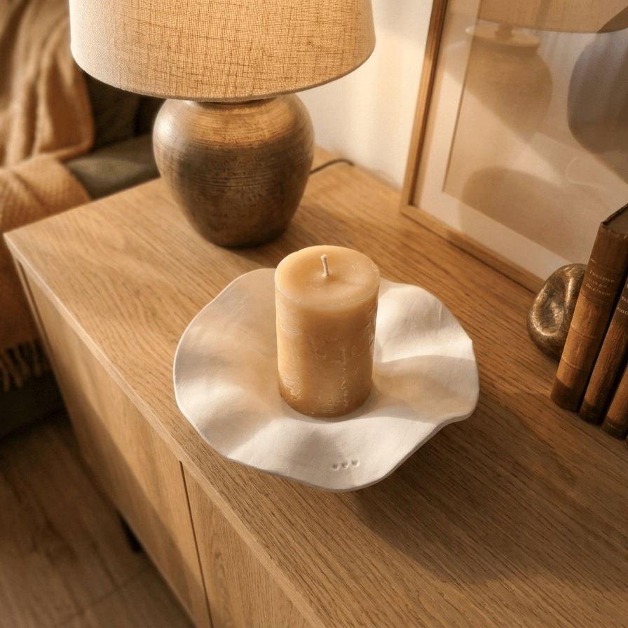 Base de cerâmica artesanal branca com bordos orgânicos, segurando uma vela cilínd